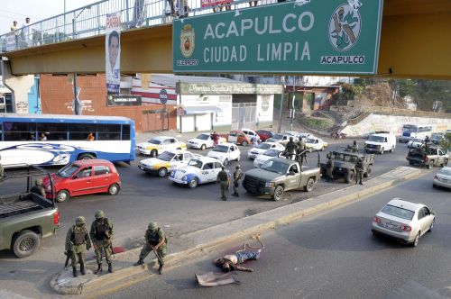 The body of a man that was hanging from a pedestrian bridge prior to the rope slipping loose is guarded by Mexican soldiers in Acapulco, Mexico, Sunday Jan. 9, 2011. Four men were found at the site, two of them decapitated and dismembered. Several separate violent incidents over the weekend in this Pacific resort city have dozens dead. Street sign on bridge reads, "Acapulco Clean City." (AP-Yonhap News)