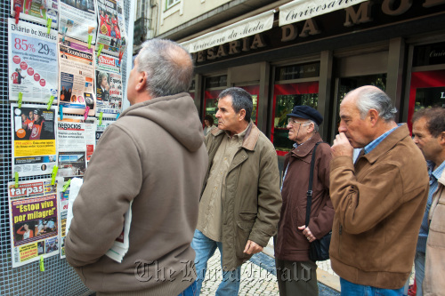 Pedestrians read the news headlines at a newspaper stand in Lisbon.  Bloomberg