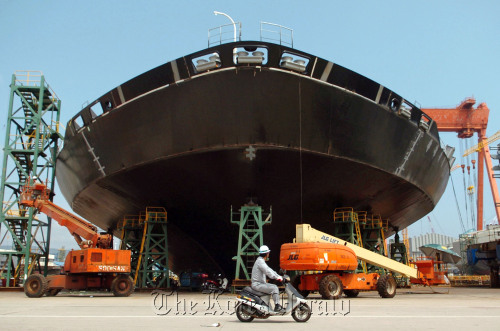 An employee rides past a container ship under construction at Hyundai Heavy Industries Co.’s shipyard in Ulsan.  Bloomberg