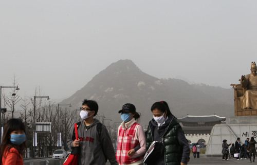 People walk on the Gwangwhamun plaza with masks on as yellow dust sweeps the nation Saturday. (Yonhap News)