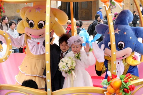 The bride Zhu Jie and her groom Qin Xueshi wave to visitors in a pumpkin carriage at their wedding held at the Discoveryland Theme Park in Dalian, Northeast China's Liaoning province, April 1, 2011. (Xinhua News)