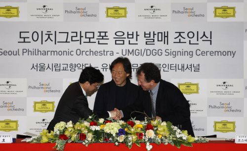 Seoul Philharmonic Orchestra music director Chung Myung-whun looks on as Universal Music Group International senior vice president Costa Pilavachi (right) and SPO CEO Kim Joo-ho shake hands after signing a long-term license agreement between the orchestra and UMGI’s Deutsche Grammophon in Seoul on Thursday. SPO