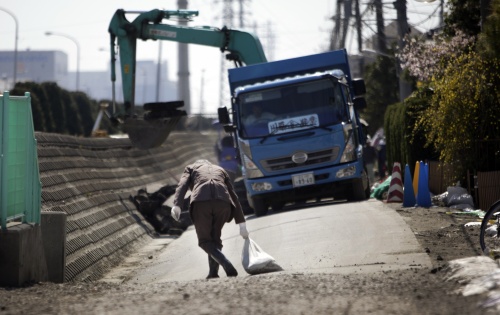 A man drags a sand bag across a street damaged by liquefaction in the March 11 earthquake in Urayasu, Chiba Prefecture, near Tokyo, Wednesday, April 6, 2011. (AP-Yonhap News)