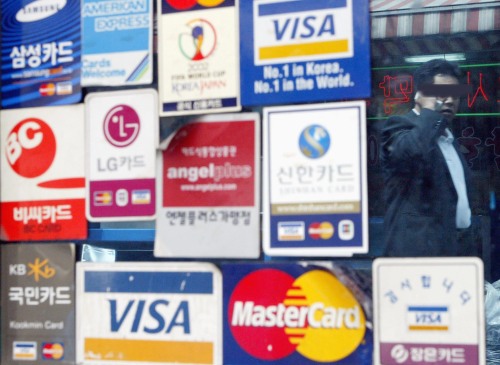 An image of a pedestrian is reflected on a window bearing stickers of various kinds of credit cards at a restaurant in Seoul May 21, 2003. South Korea's $97 billion credit card market, stimulated by tax incentives on card spending and aggressive marketing, grew about 50 percent last year after almost doubling in 2001.   REUTERS/Kim Kyung-Hoon