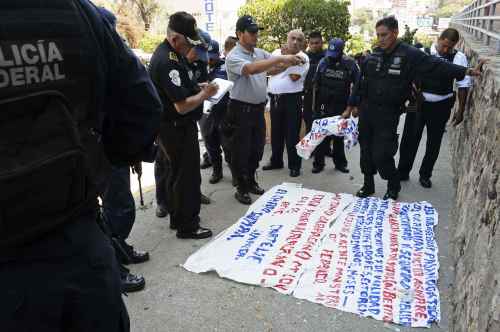 Police stand around a warning message painted on a banner left near the site where five dismembered bodies were found on the sidewalk next to a car in the Pacific resort city of Acapulco, Mexico. There are a half dozen words for drug cartel informants, and double that for drug war dead. "Narco" has become a general prefix. The trend has people worrying that Mexico is developing a kind of offhand jargon that anesthetizes people by making escalating violence seem routine. (AP-Yonhap News)