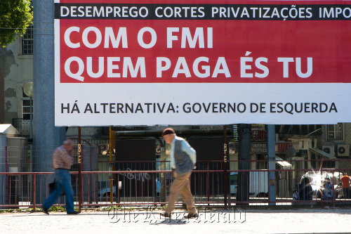 Pedestrians pass an outdoor advertisement which reads “With the IMF, it’s you who pays,” in Lisbon.  Bloomberg