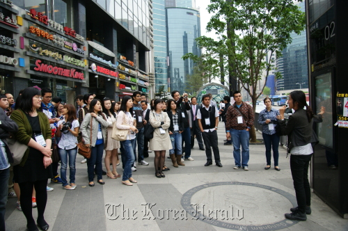 Foreign publicity ambassadors listen to a guide explaining the “media pole,” a public media art installation that functions as an information board as well as streetlight in Gangnam-daero, southern Seoul, Saturday. Gangnam-gu Office