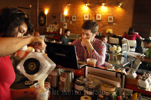 While listening to iTunes, Clay Wheeler (center) uses his laptop to catch up with theatre company work at The Pearl Cup, in Dallas, Texas.  Dallas Morning News/MCT
