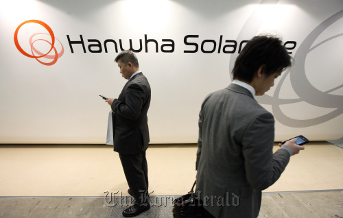 Visitors using their smartphones walk past the Hanwha Solar Holdings Co. booth at PV Expo 2011. Bloomberg