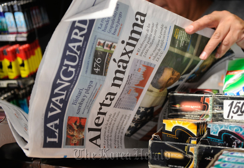 A customer reads an edition of La Vanguardia newspaper with the front page headline “Maximum Alert” about the Spanish and Italian bond crisis in Madrid.  Bloomberg