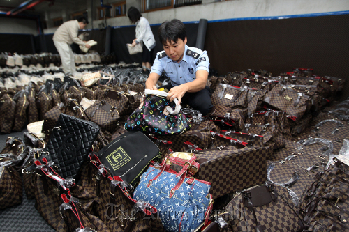 A customs official in Seoul inspects counterfeit designer goods the agency confiscated on Wednesday.  Yonhap News