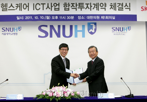 SK Telecom CEO Ha Sung-min (left) shakes hands with SNU Hospital chief Jung Hee-won after forming an agreement to establish a joint venture on health care at the hospital in downtown Seoul on Monday.        SKT