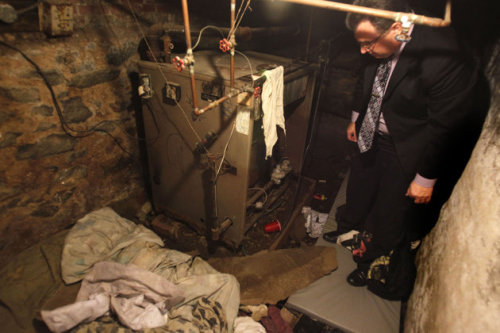 A police officer stands in the dank basement room in Philadelphia where four weak and malnourished mentally disabled adults, one chained to the boiler, were found locked inside, Monday. (AP)