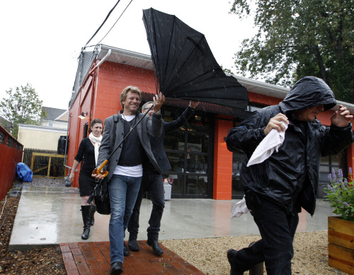 Rock star Jon Bon Jovi holds onto his umbrella in the wind and rain at the opening of his Soul Kitchen restaurant in Red Bank, N.J., Wednesday, Oct. 19, 2011.(AP)