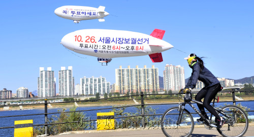 서울시 선관위는 25일 잠실 선착장 일대에서 26일 치뤄지는 서울시장 재보궐선거 투표참여를 홍보하기 위해 무인 비행선을 띄워 유권자들의 관심을 유도하고 있다.<br />김명섭 기자 msiron@
A woman riding a bicycle looks at an airship to promote the Oct. 26 Seoul mayoral by-election in Seoul on Tuesday.   Kim Myung-sub/ The Korea Herald