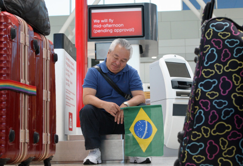 A stranded Qantas Airways Ltd. traveler holding a Brazilian flag sits in the domestic terminal at Sydney Airport in Sydney, Australia, on Monday. (Bloomberg)