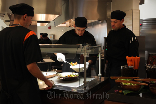 Assistant cooks Jose Espenoza (center) and Moses Mendez (right) work behind the counter to serve up a dish of Thai stir fry pork with long beans at UCLA’s new dining hall.    Los Angeles Times/MCT
