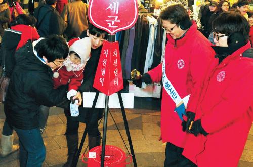 A family puts a bill into a Salvation Army red kettle in Myeongdong, Seoul, on Thursday. (Park Hyun-koo/The Korea Herald)