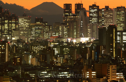 Mount Fuji, Japan’s highest peak, emerges through buildings in the Shinjuku district at dusk, in Tokyo.  Bloomberg