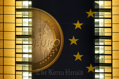 A giant euro banner, featuring an image of a euro coin and promoting stronger European economic governance, is illuminated at night as it hangs on the side of the headquarters of the European Union commission at the Berlaymont Building, in Brussels.  Bloomberg