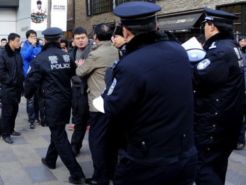 Chinese police detain a man after customers scuffled, threw eggs at the glass front of the Apple store in Beijing's upmarket Sanlitun shopping district on January 13, 2012. (AFP)