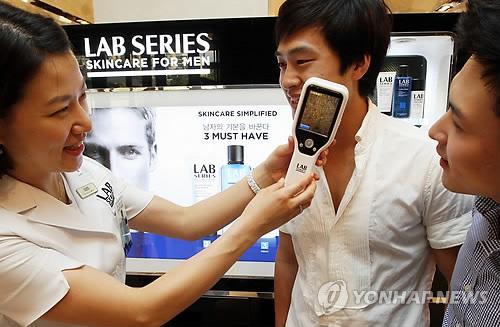 Men receive skincare counseling at a department store cosmetics counter.  Yonhap News