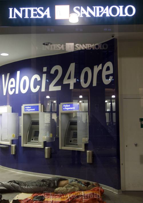 A homeless man sleeps inside the withdrawal area of a Intesa Sanpaolo bank in downtown Milan on Feb. 9, 2012. (Reuters-Yonhap News)
