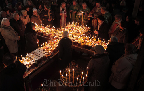 Bulgarian Orthodox priests read prayers as people gather around candles stuck to jars of honey arranged as a Holy Cross in Blagoevgrad, Bulgaria, Feb. 10. (AP-Yonhap News)