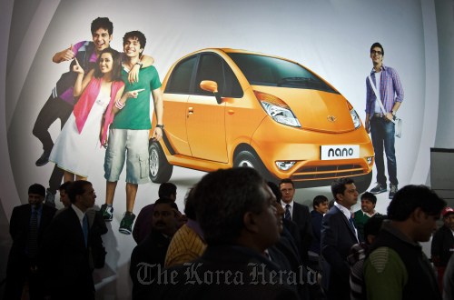 Crowds stand in front of an advertisement for Tata Motors Ltd.’s Nano hatchback vehicle at the Auto Expo 2012 in New Delhi.  Bloomberg