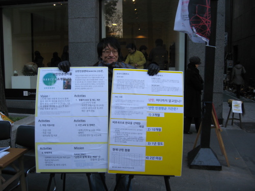 NANCEN program manager Choi Won-geun holds up a poster during a previous campaign to support asylum seekers and refugees in Korea.   NANCEN