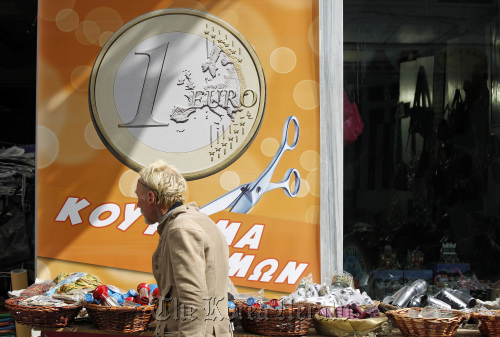A pedestrian passes a euro coin advertisement which reads “prices haircut” in Athens on Wednesday.  Bloomberg