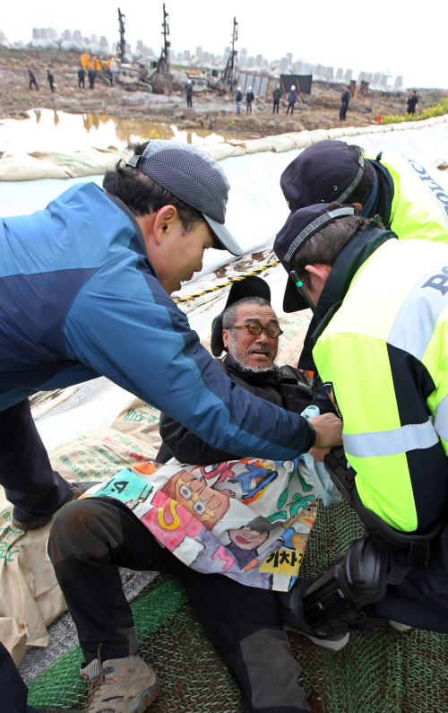 <YONHAP PHOTO-0826> 해군기지 공사장 들어간 문규현 신부 (제주=연합뉴스) 김호천 기자 = 9일 오전 제주도 서귀포시 강정마을 해군기지 공사장 펜스를 뜯어내고 안으로 들어갔던 문규현 신부가 경찰에 연행되고 있다. 2012.3.9. khc@yna.co.kr/2012-03-09 14:31:27/ <저작권자 ⓒ 1980-2012 ㈜연합뉴스. 무단 전재 재배포 금지.>
Catholic priest Moon Gyu-hyun is taken away by the police after he broke a fence around the naval base construction site to enter the premises on Jeju Island on Friday.  Yonhap News