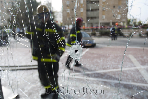 Israeli firefighters are seen through a shattered window after a rocket fired by Palestinian militants from the Gaza Strip hit the city of Ashdod, Israel, Monday.  AP-Yonhap News