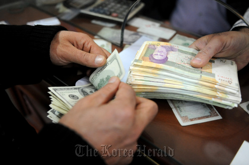 A currency trader prepares to exchange Iranian rial notes (right) for U.S. dollar notes at a currency exchange in Tehran.  Bloomberg