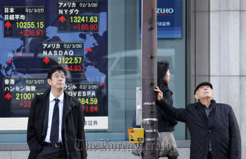 Pedestrians wait to cross a road in front of an electronic stock board outside a securities firm in Tokyo.  Bloomberg