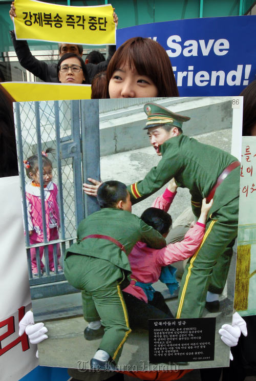 A woman holds a photo, entitled “Cries of North Korean defectors,” during a rally in Seoul last month. The photo shows a North Korean defector being captured after attempting to enter a South Korean mission in China.   Yonhap News
