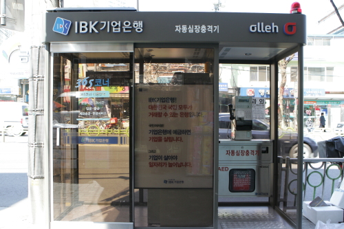 자동심장충격기(AED)와 현금자동입출금기(ATM)가 설치된 공중전화가 있어 눈길을 끌고 있다.  서울시 성동구는 KT링커스, IBK기업은행과 협약을 맺고 금남시장 인근 금호동 로터리에 ‘결합형 공중전화부스’를 설치했다고 9일 밝혔다. 새롭게 선보이는 공중전화부스는 공중전화와 자동심장충격기가 설치되고 또 다른 공간에는 현금자동입출금기가 놓여진다.  [사진제공=성동구]