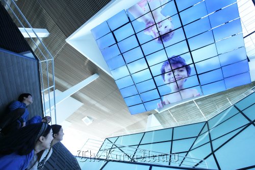 Visitors look at LG’s media chandelier, composed of 54 display panels, which shows dynamic artwork accompanied by sound at its building constructed for the Expo 2012 in Yeosu on Sunday.  LG Group