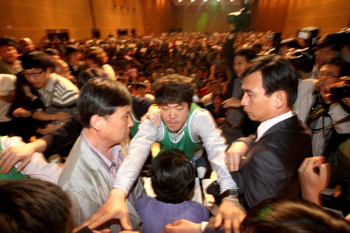 <YONHAP PHOTO-0859> 심상정 의장을 보호하라 (고양=연합뉴스) 백승렬 기자 = 통합진보당 중앙위원회 심상정 의장이 12일 고양시 킨텍스에서 열린 제1차 중앙위원회의에서 강령개정을 통과시키고 나서 단상에 난입한 중앙위원과 당원들의 공격을 받자 유시민 조준호 공동대표와 행사진행요원이 에워싸고 있다. 2012. 5. 12 srbaek@yna.co.kr/2012-05-12 22:21:51/ <저작권자 ⓒ 1980-2012 ㈜연합뉴스. 무단 전재 재배포 금지.>
Rhyu Si-min (in dark suit), former co-chair of the Unified Progressive Party, attempts to protect his colleague Sim Sang-jeong (center, facing away) from the violent attacks of the mainstreamers during the party’s central committee meeting on Saturday.  Yonhap News