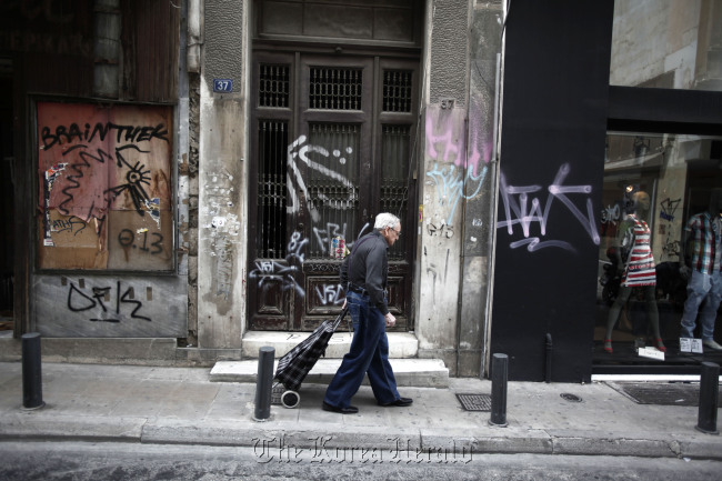 A pedestrian wheels a shopping trolley past a graffitied building in Athens.  Bloomberg