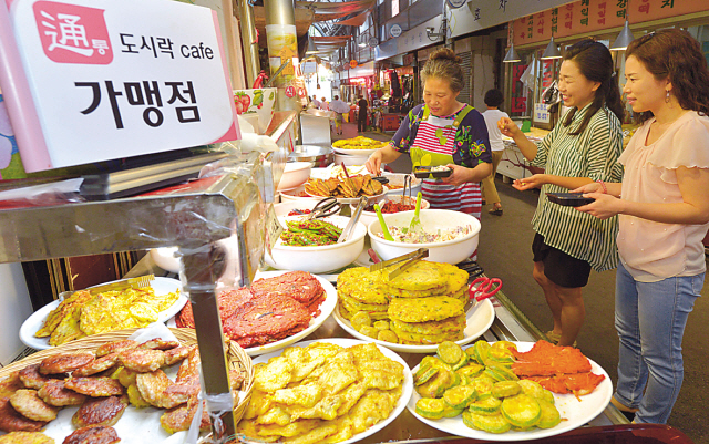 Two staff members at Tongin Market Dosirak Cafe demonstrating brass yeopjeon coins used to buy banchan side dishes at affiliate stalls