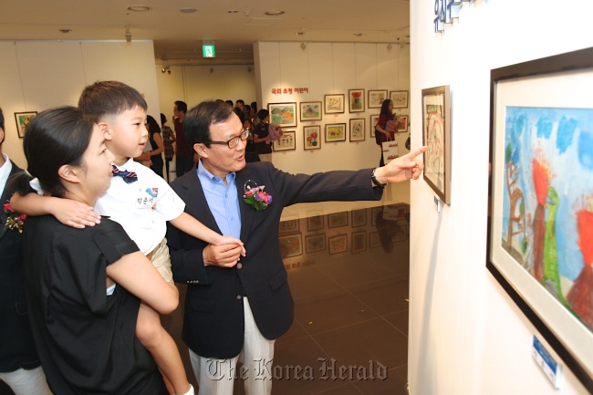 Woori Bank CEO Lee Soon-woo (right), along with a child winner and his mother, looks at the work that won the grand prize in the drawing competition organized by the lender on Saturday.  (Woori Bank)