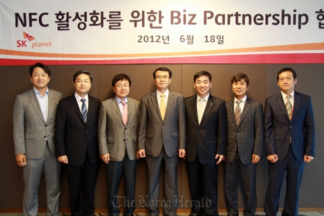 Kim Soo-il (center), senior vice president of SK Planet’s commerce business unit, poses with other executives from the company’s six business partners after forming an alliance to promote NFC-based mobile payment.