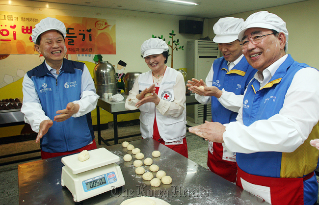 Shinhan Financial Group chairman Han Dong-woo (right) and the group’s executives make bread and noodles in Seoul to be given to low-income families.  Shinhan Financial