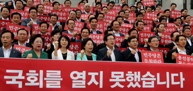 Saenuri Party lawmakers hold up banners and chant slogans urging an immediate opening of the 19th National Assembly in front of the Assembly’s main building on Tuesday.    Yonhap News