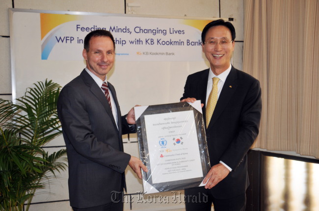 KB Kookmin Bank chief executive Min Byong-deok (right) poses with Jean-Pierre de Margerie, director of World Food Program in Cambodia, after delivering donations for a school meals program in impoverished areas on Wednesday in Phnom Penh. Min was in Vietnam and Cambodia to check on KB Kookmin’s local units and meet with Korean businesses there.  (KB Kookmin Bank)