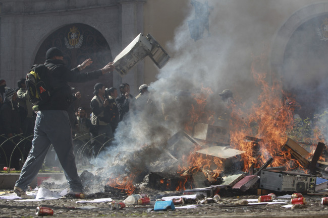 A police officer demanding a salary increase tosses a computer onto a bonfire outside a police internal affairs building, in La Paz, Bolivia, Friday.   (AP-Yonhap News)