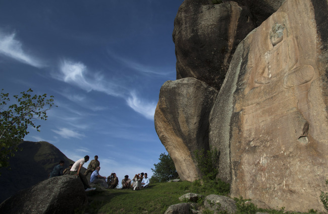 In this May 24 photo, people sit near a sculpture of the Buddha whose face was destroyed by Taliban fighters at Jahanabad, Pakistan, in the Swat valley. (AP-Yonhap News)