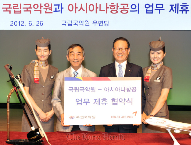 Asiana Airlines CEO Yoon Young-doo (second from right) and National Gugak Center director general Lee Dong-bok pose with Asiana flight attendants after signing a memorandum of understanding in Seoul on Tuesday. The MOU focuses on promoting gukak, or Korean traditional music, at home and overseas, such as offering gukak lessons to foreign visitors and children.  (Asiana Airlines)
