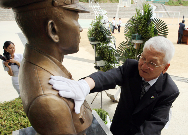 Yoon Du-ho, father of Lt. Cmdr. Yoon Young-ha, touches the bust of his son on Thursday at the Songdo High School in Incheon where he graduated. The officer is one of the six killed by a North Korean naval attack on June 29, 2002. (Yonhap News)
